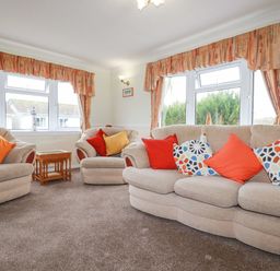A living room with two beige armchairs and a beige sofa with cushions and curtains at Summer Breeze in Tregolds near St Merryn