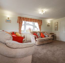 A living room with two beige sofas with colorful cushions and orange curtains at Summer Breeze in Tregolds near St Merryn