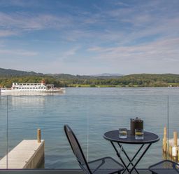 A lake view with a boat on the water and two chairs and a table with drinks on a balcony at Boathouse on the Lake in Bowness-On-Windermere