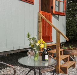 An outdoor seating area with a glass top table holding flowers a wine bottle and an upside down glass near wooden steps and a door at Ewes Welcome in Cottingham