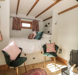 A small bedroom with a bed, two chairs with cushions, floral curtains, a wood-burning stove, and wooden beams at Ewes Welcome in Cottingham