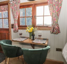 A small dining area with a wooden table set with two wine glasses and a bottle between two green chairs by a window with floral curtains at Ewes Welcome in Cottingham