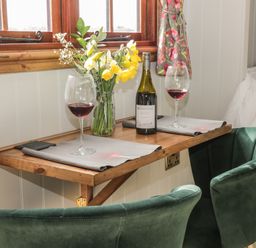 A small wooden table with two green chairs red wine glasses wine bottle and flowers by a window at Ewes Welcome in Cottingham
