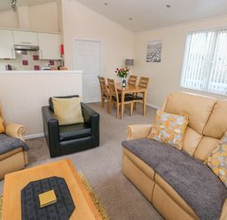 A living room with beige sofa black armchair dining table and kitchen area at The Hideaway - Heritage Park in Stepaside near Kilgetty
