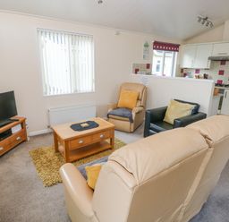 A living area with a beige leather sofa and armchairs a wooden coffee table a television on a wooden stand and an open kitchen at The Hideaway - Heritage Park in Stepaside near Kilgetty