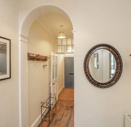 A hallway with a wooden floor a round wall mirror a brass bell a framed picture and a metal shoe rack at Seasides in Weymouth