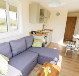 A small living area with a gray sectional sofa and green pillows next to a compact kitchen with wooden countertops at Malvern View Lodge in Wadborough near Pershore