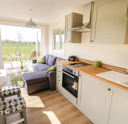 A kitchen and living area with wooden countertop oven sofa and stools leading to an outdoor seating area at Malvern View Lodge in Wadborough near Pershore