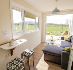 A small living area with a sofa table with cups stools and an open door leading to a patio and field at Malvern View Lodge in Wadborough near Pershore