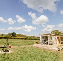 A wooden lodge with outdoor seating and a fire pit in a grassy field at Malvern View Lodge in Wadborough near Pershore