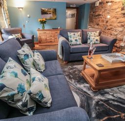 A sitting room with sofas cushions a wooden coffee table floor lamp and exposed stone wall at Granary Cottage in Bellingham