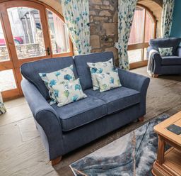 A living room with blue armchairs and loveseat with floral cushions near arched wooden doors at Granary Cottage in Bellingham