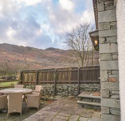 An outdoor patio area with a round table and six chairs next to a stone wall and wooden fence with hills in the background at Plumblands in Chapel Stile