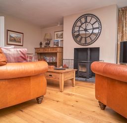 A living room with two leather sofas a wooden coffee table a fireplace with a protective screen a large wall clock and a wooden cabinet at Plumblands in Chapel Stile