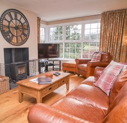 A living room with leather sofa and armchair a wooden coffee table a large wall clock and a television by the window at Plumblands in Chapel Stile