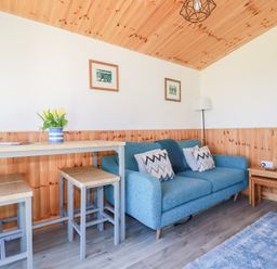 A living room with a blue sofa table and stools with flowers on the table at 194 Atlantic Bays in Atlantic Bays Holiday Park near St Merryn