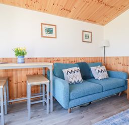 A living area with a blue sofa and patterned cushions a wooden table with stools and a vase of yellow tulips at 194 Atlantic Bays Atlantic Bays Holiday Park near St Merryn