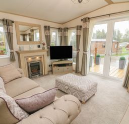A living room with sofas a fireplace a television and glass doors at Lancaster Lodge in South Lakeland Leisure Village