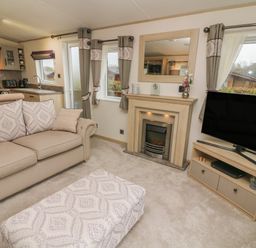 A living room with a sofa ottoman fireplace and television at Lancaster Lodge in South Lakeland Leisure Village