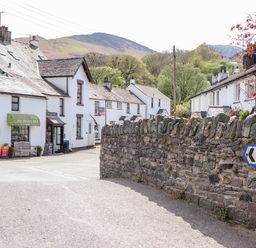 Village street with white houses a stone wall and a shop with a green awning at Holme Rigg in Braithwaite