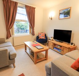 A living room with two sofas a blue armchair a wooden coffee table a TV on a wooden stand and curtains at Holme Rigg in Braithwaite