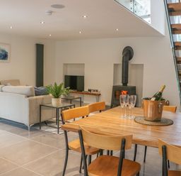 A dining area with wooden table and chairs adjacent to a living room with a sofa a wood stove and stairs at Fig Cottage in Kirkby Stephen