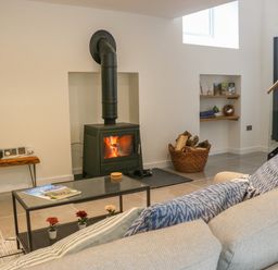 A living room with a wood burning stove a glass coffee table a light sofa and a basket of firewood at Fig Cottage in Kirkby Stephen