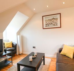 A living room with a television on a stand a black coffee table with cups and a plant and sofas with yellow cushions at Harbour Reach 6 in Weymouth