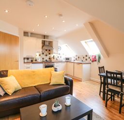 A kitchen and dining area with a brown sofa and yellow cushions at Harbour Reach 6 in Weymouth