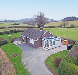 A single-story house with a driveway and surrounding hedges in a rural setting at Berwyn View in Trelydan near Welshpool