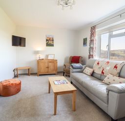 A living room with a grey sofa a wooden coffee table an armchair a wall-mounted TV and a window showing a rural view at Berwyn View Trelydan near Welshpool