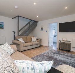 A living room with two sofas a staircase a wall-mounted television and a door leading to a kitchen at Beach Cottage in Portreath