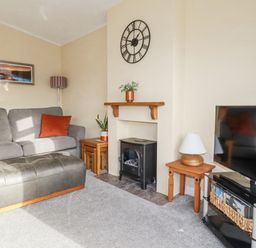 A living room with a grey sofa orange cushions a black ottoman and a television at Laurel Lodge Bossiney Bay Holiday Park near Tintagel