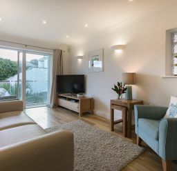 A living room with a beige sofa blue armchair wooden TV stand and sliding glass door at Atlantis in St Ives