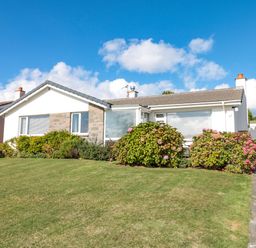 A single story house with shrubs and grass lawn at 33 Weymouth Park in Hope Cove