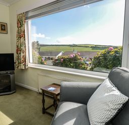 A sitting area with a gray armchair and polka dot pillow next to a window with floral curtains and a TV on a stand at 33 Weymouth Park in Hope Cove