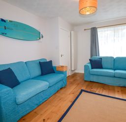 A living room with two blue sofas a surfboard mounted on the wall and a window with curtains at Estuary View in Newquay