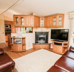 A living room with two brown leather sofas a white rug a television and wooden cabinets at The Lodge in Pontyates