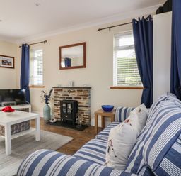 A living room with a striped sofa a coffee table a television and a fireplace at Hazel Cottage in Tintagel