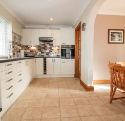 A kitchen with white cabinets a tiled floor and a wooden dining table with chairs at Hazel Cottage in Tintagel
