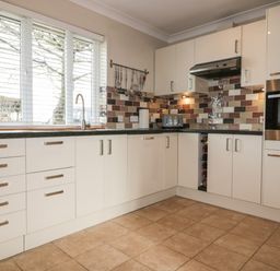 A kitchen with white cabinets a tiled floor a window with blinds and kitchen appliances at Hazel Cottage in Tintagel