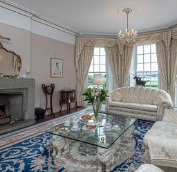 A living room with a fireplace glass coffee table and floral carpet at Tal Gwynedd in Dwyran near Newborough