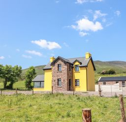 A yellow house with stone accents and a detached stone building in a grassy area at Lack Cottage Annascaul near Camp County Kerry