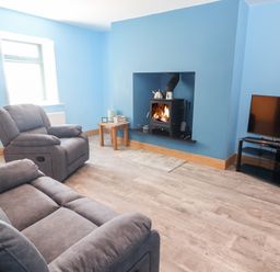 A living room with gray sofas a wood burning stove a small wooden table and a television on a stand at Lack Cottage Annascaul near Camp County Kerry
