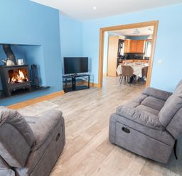 A living room with two gray recliner chairs a wood stove and a TV facing a dining area with a table and chairs at Lack Cottage Annascaul near Camp County Kerry