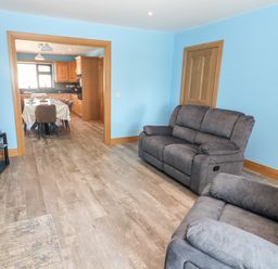 A living room with two gray sofas and a television showing a kitchen and dining area at Lack Cottage in Annascaul near Camp County Kerry