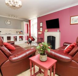 A living room with two red leather chairs a small red table with a plant a wall-mounted TV and a kitchenette at The Tack Room in Lydney