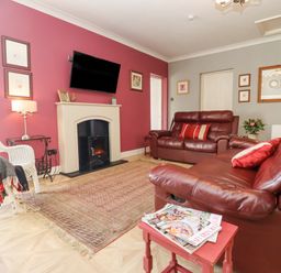 A living room with red walls two leather sofas and a television above a fireplace at The Tack Room in Lydney