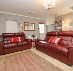 A living room with two red leather sofas a patterned rug a bookshelf and a window at The Tack Room in Lydney