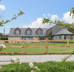 A stone house with a slate roof and wooden fence with green lawn and flowering tree branches at Higher Kernick View Helland near Blisland